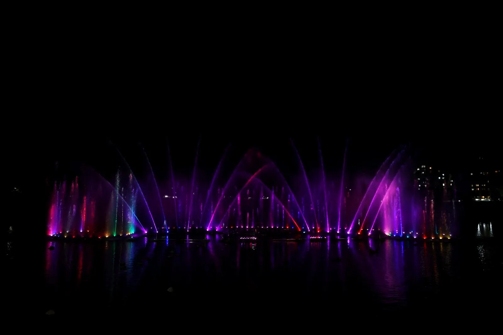 A floating fountain show at night, with violet and magenta jets over black water
